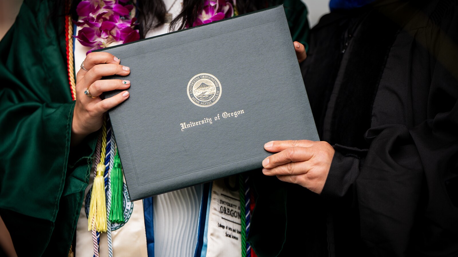 A graduate holds a University of Oregon diploma.