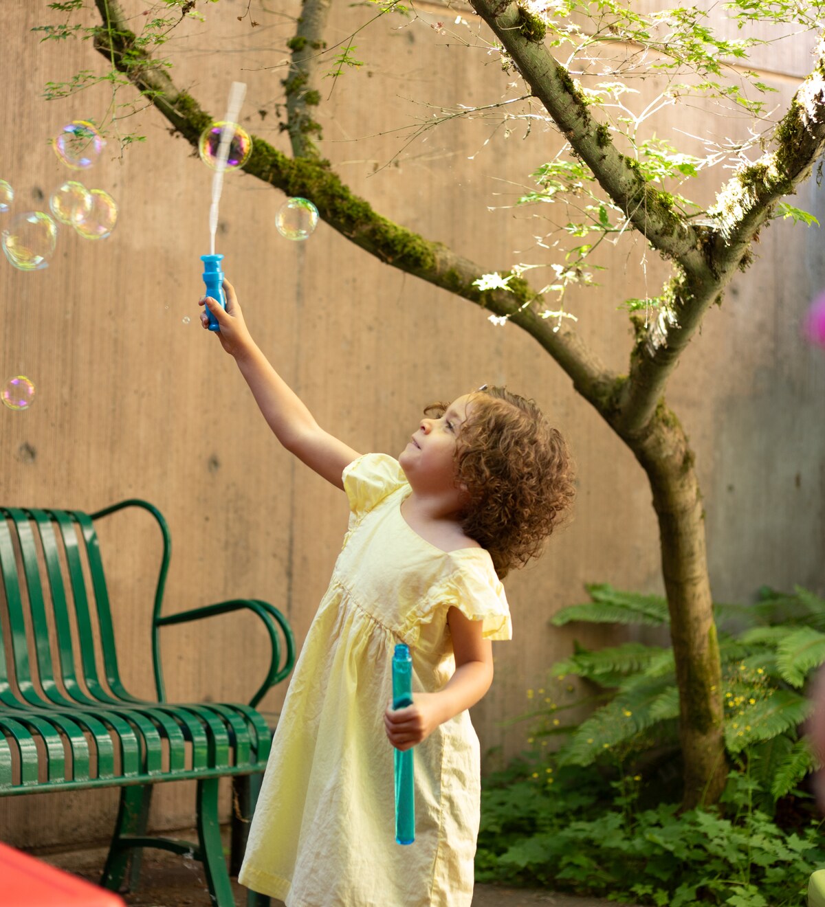 A child blows bubbles beneath a tree.