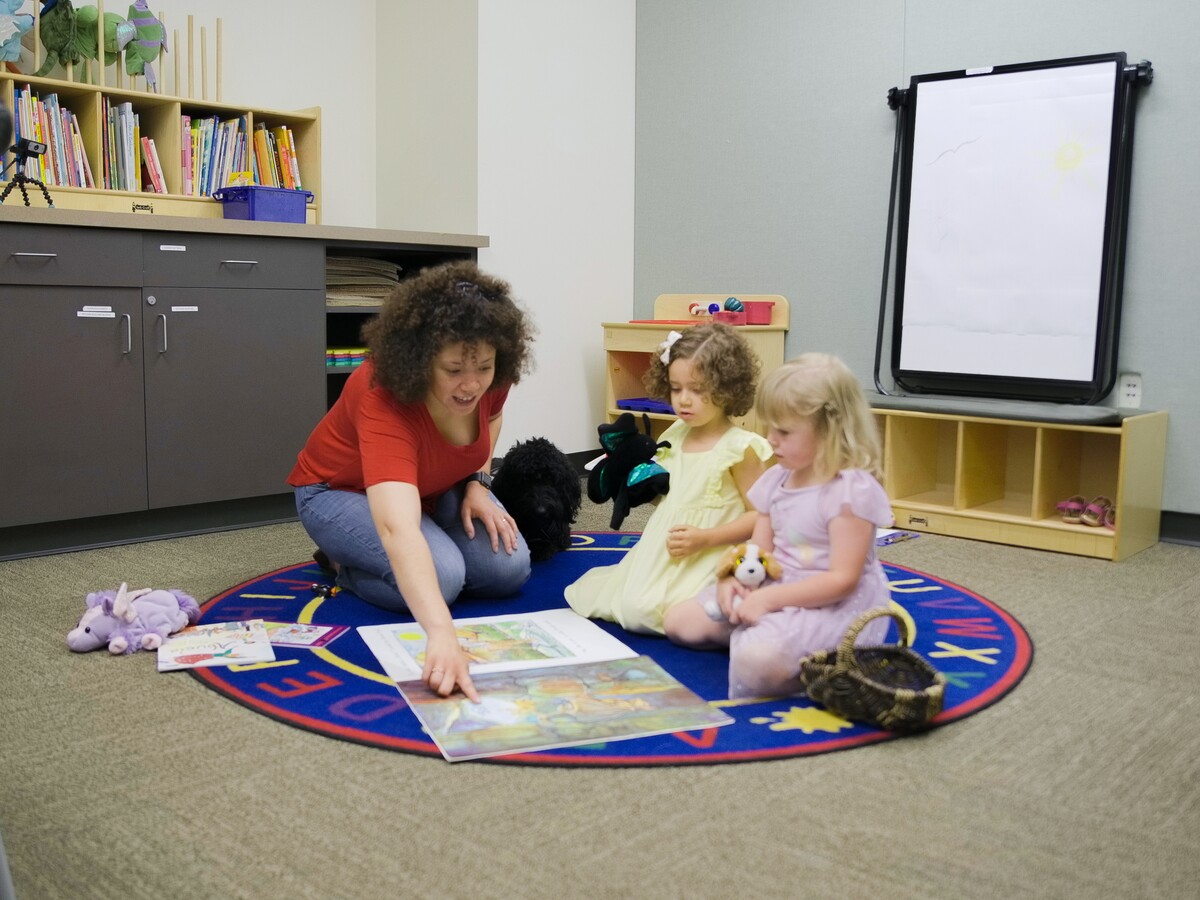 An adult reads with two children in a playroom.
