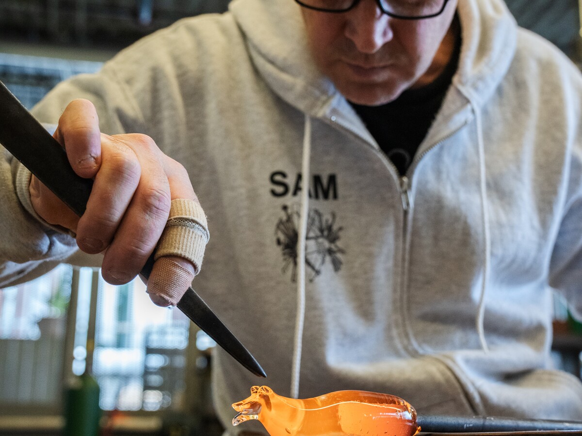 A person shapes molten glass at the Craft Center.