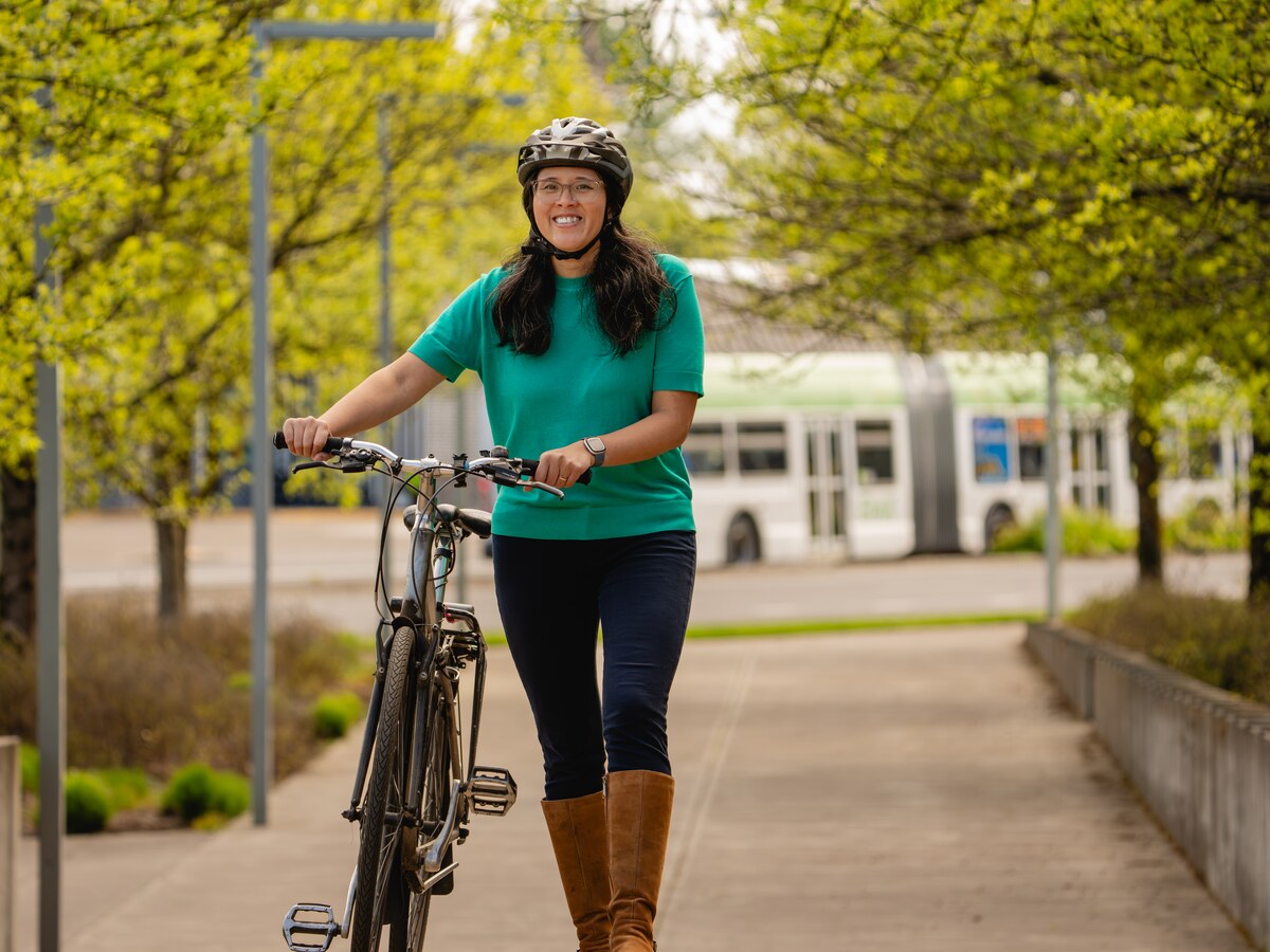 A student walks a bicycle along a campus path.