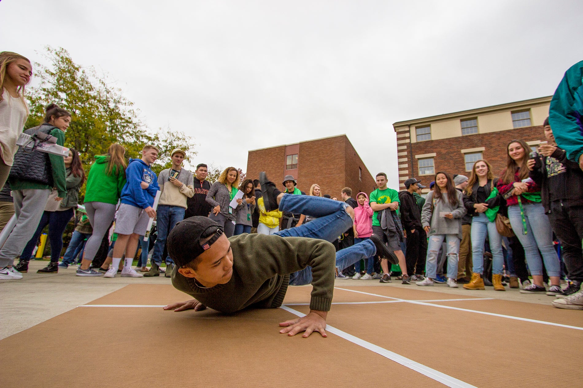 A student breakdances in the middle of a crowd.