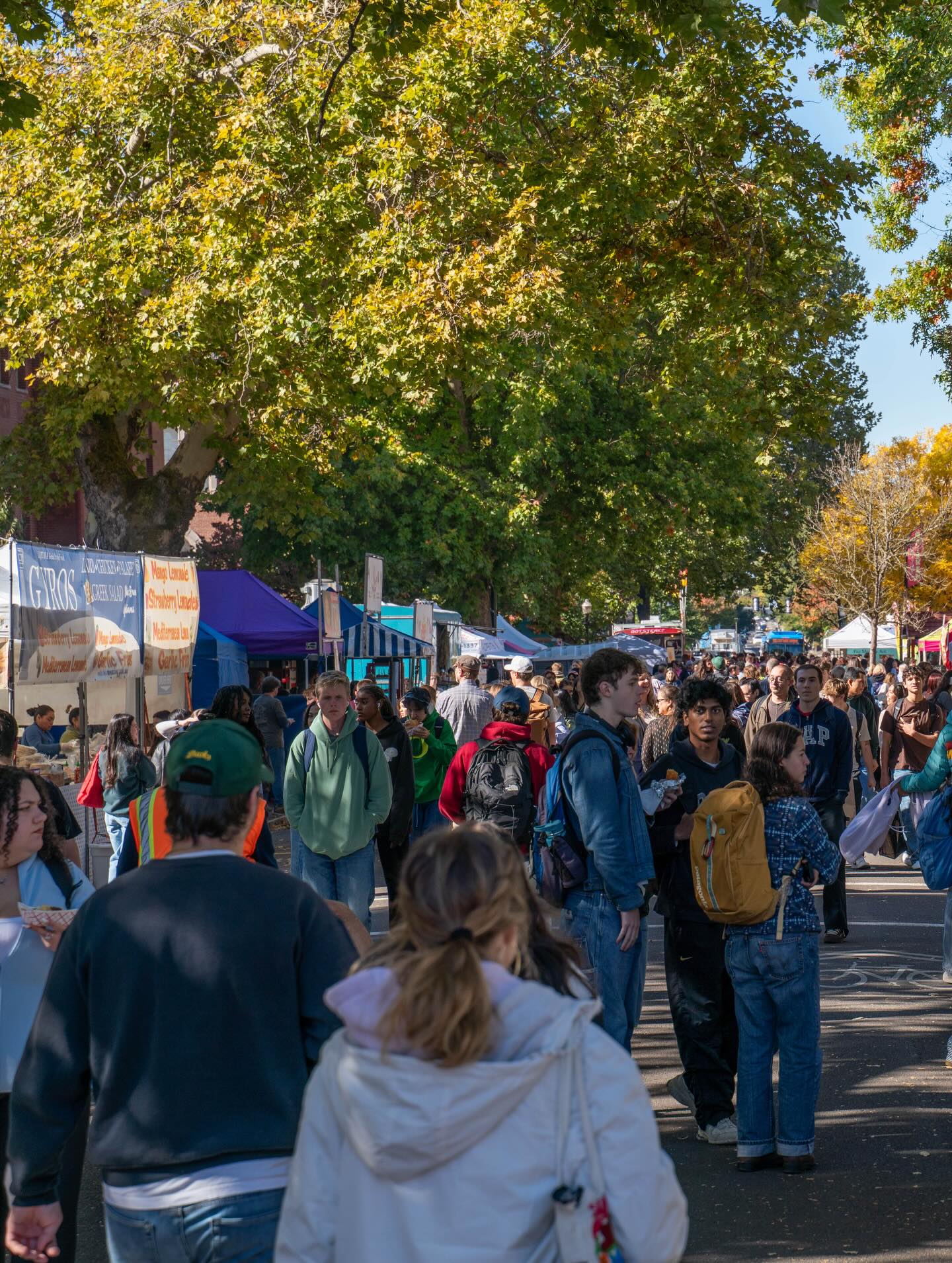 A crowd walks among food stalls at an outdoor market in Eugene.