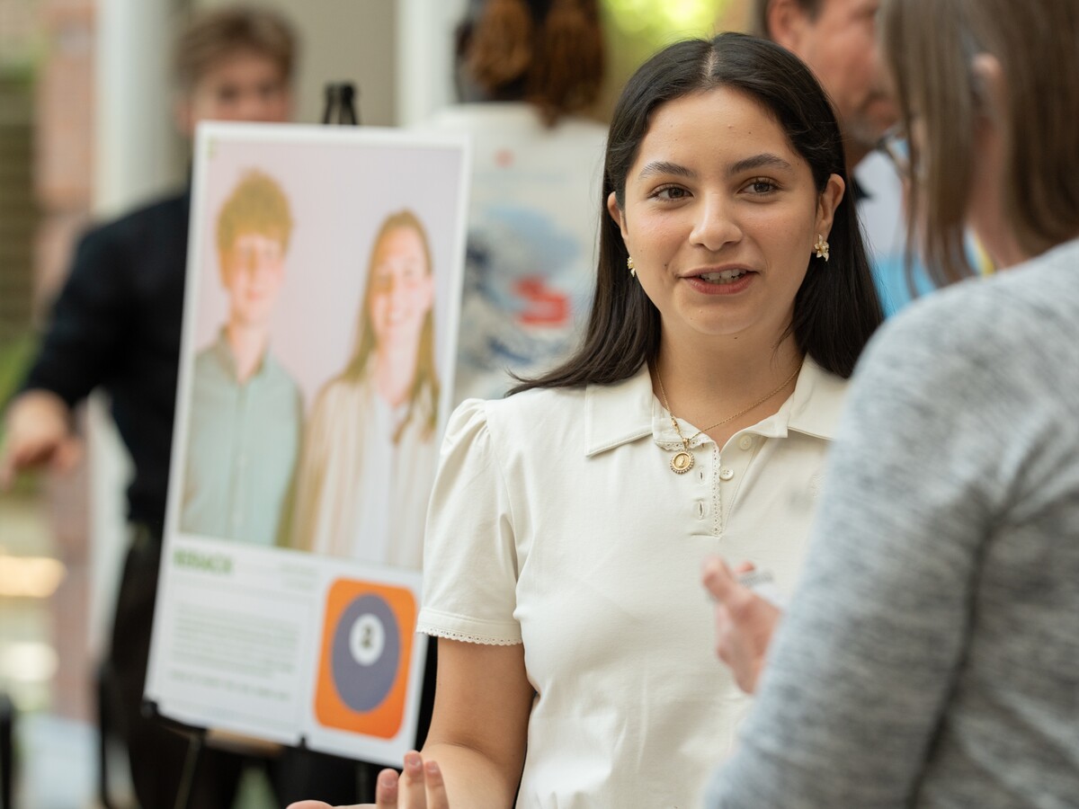 A presenter discusses a research poster at a technology event.