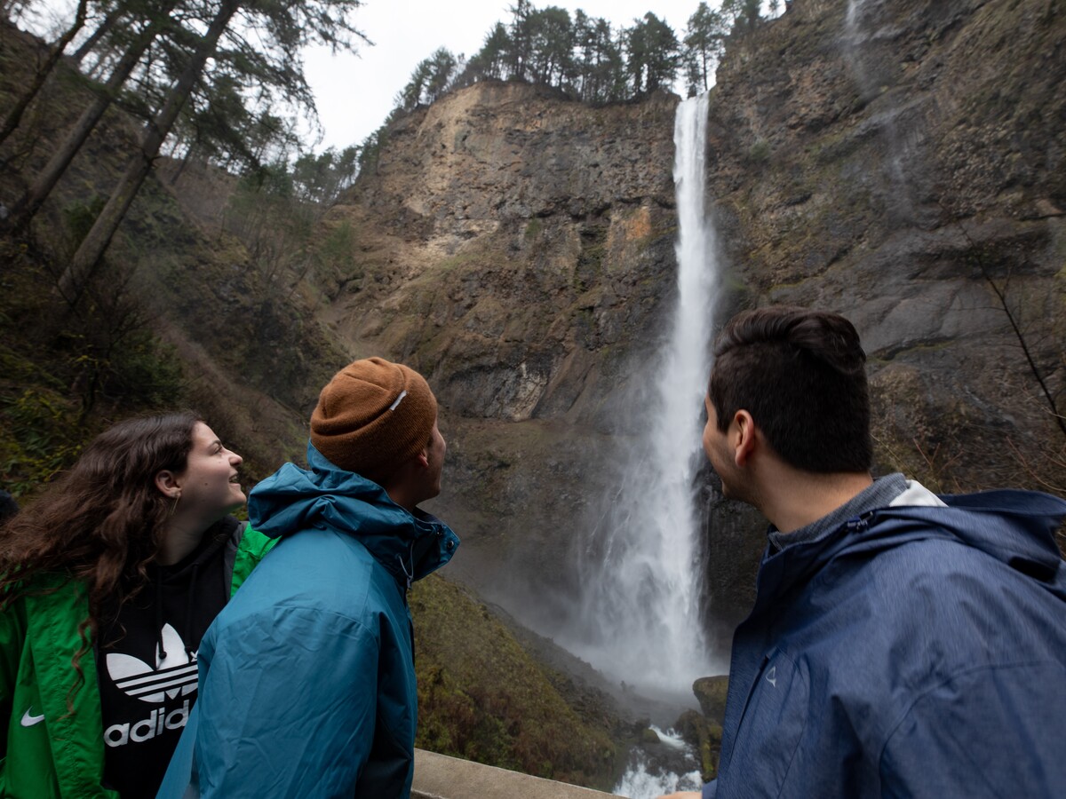 Three people look toward a waterfall in the Columbia River Gorge.
