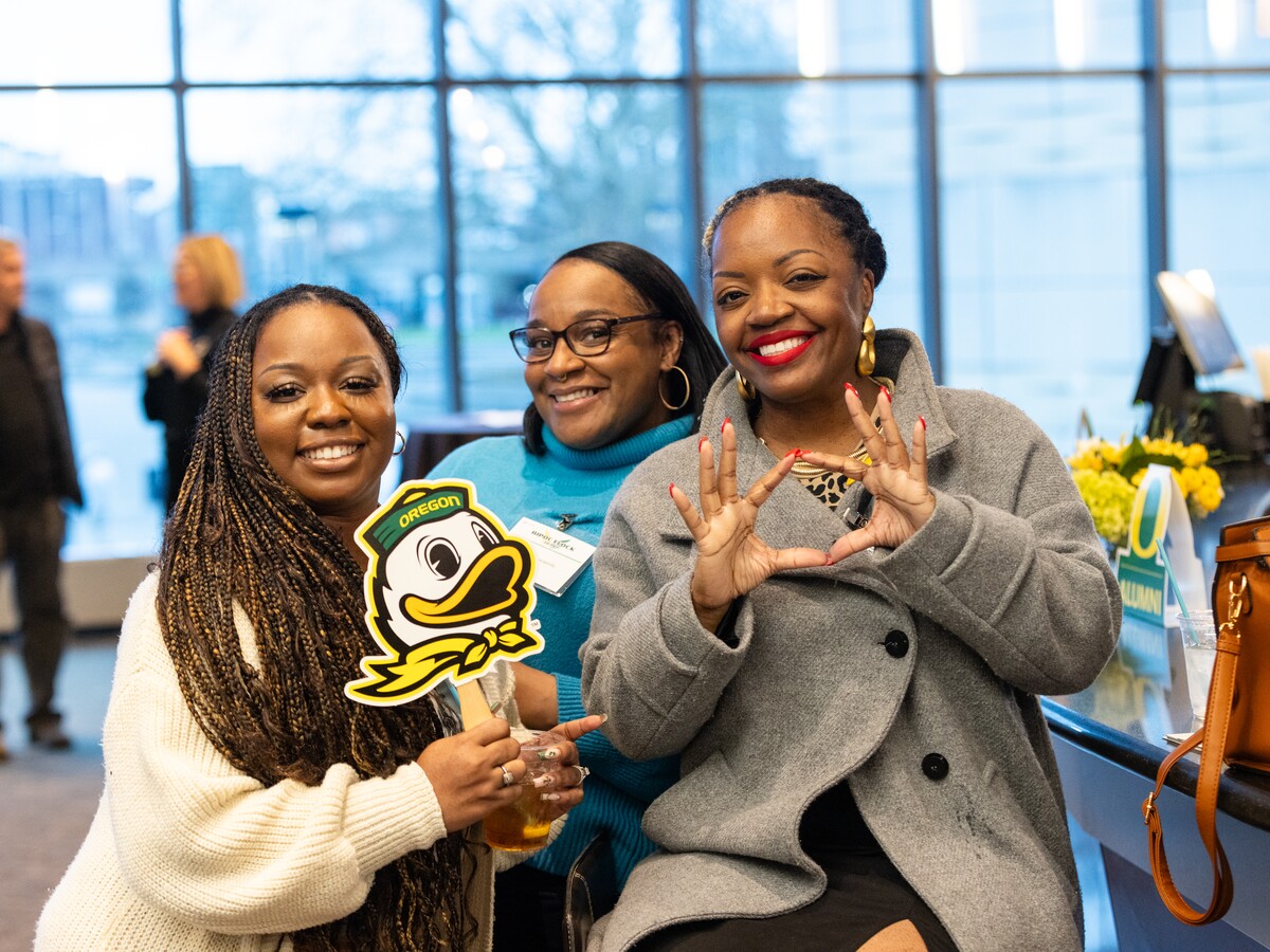 Alumni pose with Oregon Duck signs at an event.