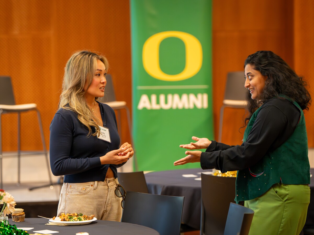 Two alumnae talk beside an Oregon Alumni banner.